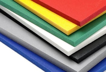 Planchas de PVC espumado apiladas, en rojo, amarillo, verde, blanco, negro, gris y azul, con el canto a la vista